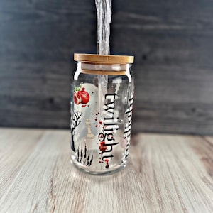 May include: A clear glass jar with a wooden lid and a black and white design featuring the word "twilight" and a red pomegranate. The jar is filled with a clear liquid and a clear plastic straw.