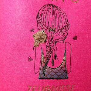 Puede incluir: Un artículo de fieltro rosa intenso con texto bordado en oro que dice "LENA'S" y "ZEUGNISSE". Presenta un dibujo lineal negro de una niña con una trenza larga, un pequeño osito de peluche y formas de corazón.