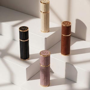 Peut inclure: Quatre atomiseurs de parfum cylindriques en noir, crème, marron et mauve, chacun doté d'un extérieur texturé, d'une garniture en métal doré et d'un capuchon circulaire gravé des lettres SH avec une finition dorée.