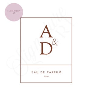 May include: A rectangular perfume label with a brown border featuring the letters A and D separated by an ampersand in the center. Below, the text reads EAU DE PARFUM and 30ML. A small light purple circle in the top left corner contains LABEL OPTION #5.