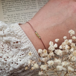 May include: A brown string bracelet with three small green and gold beads.