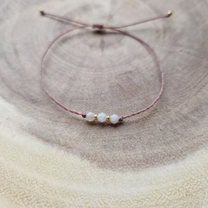 May include: A simple bracelet with a brown cord and three white gemstone beads.