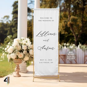 May include: A white wedding welcome sign on a gold stand. The sign reads "Welcome to the Wedding of Lillian and Aaron" with the date and location below. A floral arrangement and outdoor setting are in the background.