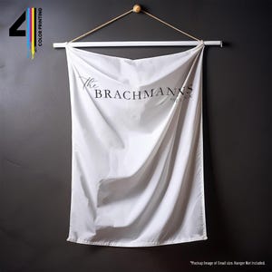 Pu&ograve; includere: Un arazzo da parete bianco con la scritta "The Brachmanns" in nero. Lo striscione &egrave; sospeso da un dowel di legno e una corda naturale. L'angolo in alto a sinistra ha il numero "4" con stampa a colori.