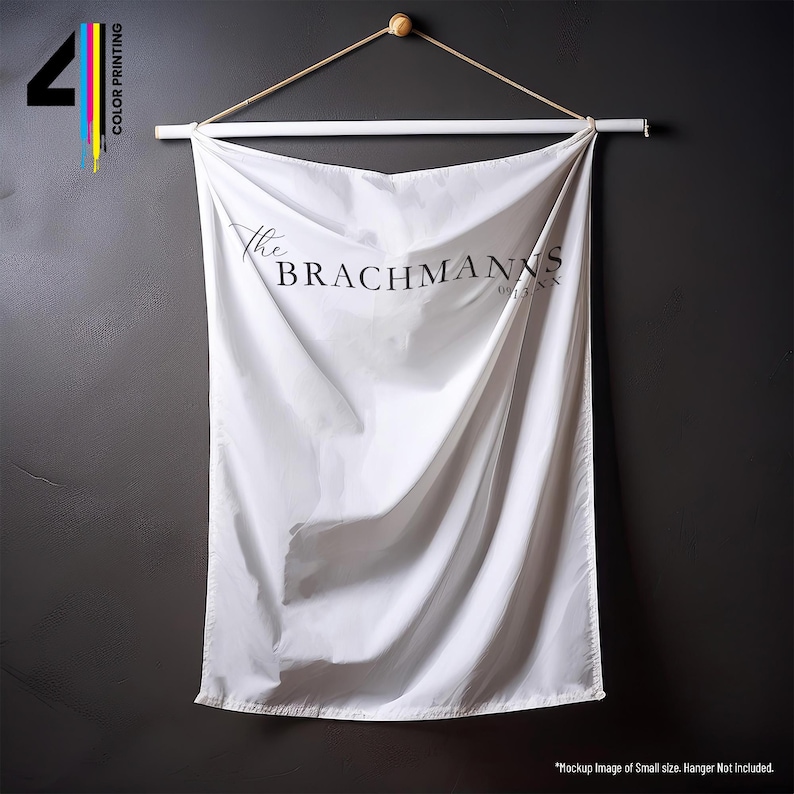 Pu&ograve; includere: Un arazzo da parete bianco con la scritta "The Brachmanns" in nero. Lo striscione &egrave; sospeso da un dowel di legno e una corda naturale. L'angolo in alto a sinistra ha il numero "4" con stampa a colori.