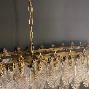 May include: An antique brass chandelier with clear, fan-shaped glass panels. The rectangular frame is adorned with ornate brass detailing and suspended by chains. The design features a vintage aesthetic, suitable for interior lighting.