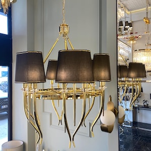 May include: A gold chandelier with black fabric shades and curved arms. The chandelier has a circular base and is hanging from the ceiling.