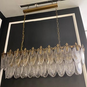 May include: A rectangular chandelier with a gold-colored frame and chains. The chandelier features multiple clear, oval-shaped glass elements with a textured design. The fixture is suspended from the ceiling, showcasing a modern lighting design.