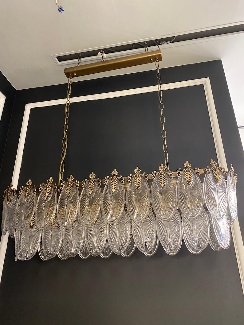 May include: A rectangular chandelier with a gold-colored frame and chains. The chandelier features multiple clear, oval-shaped glass elements with a textured design. The fixture is suspended from the ceiling, showcasing a modern lighting design.