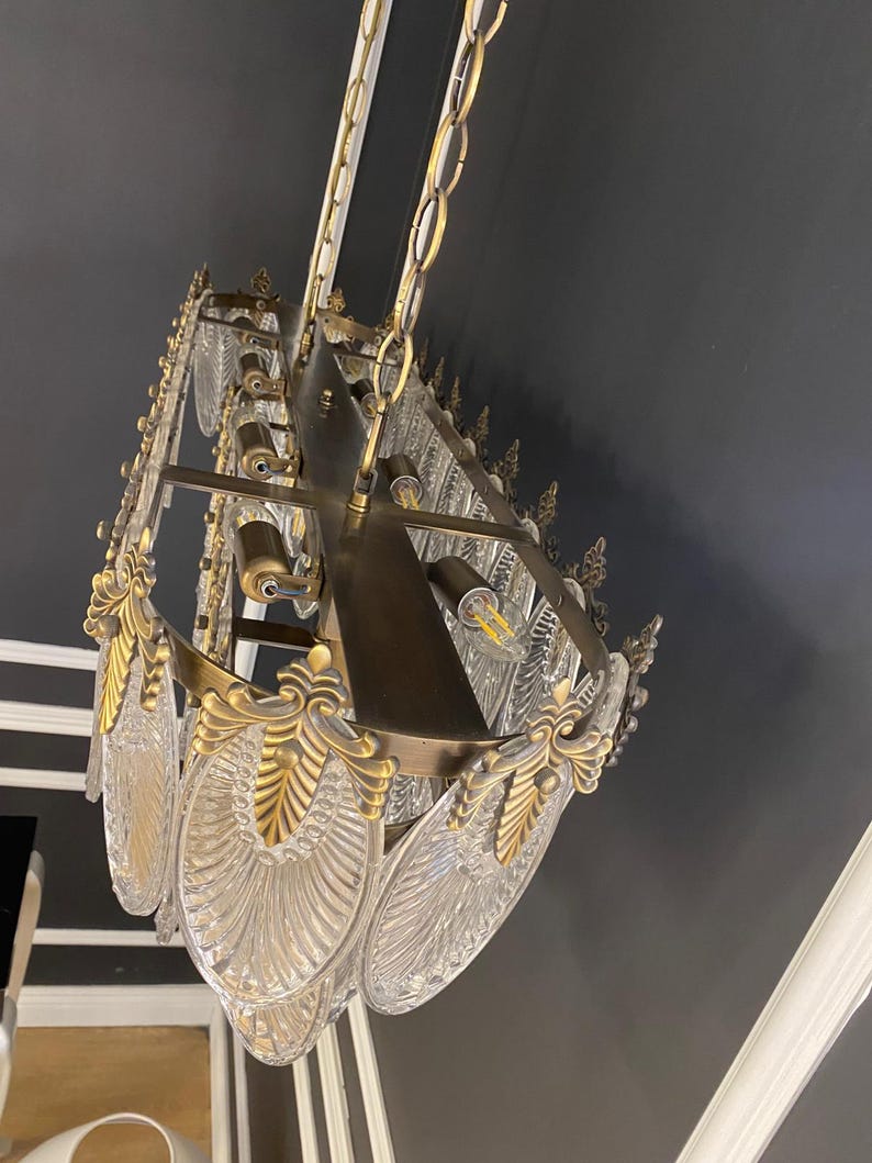 May include: An ornate chandelier with a brass frame and clear, leaf-shaped glass panels. The fixture is suspended from a chain and features decorative gold accents. The chandelier is mounted on a dark gray ceiling.