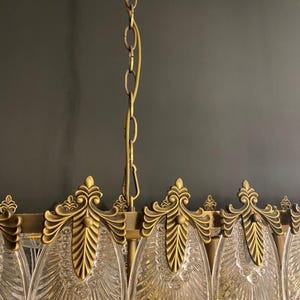 May include: Close-up of a vintage chandelier with a brass finish and clear glass elements. The chandelier features ornate, leaf-like details and a hanging chain. The design is elegant and suitable for interior lighting.