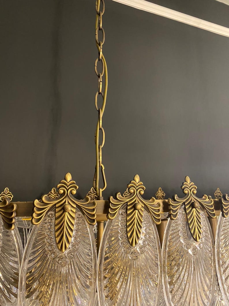 May include: Close-up of a vintage chandelier with a brass finish and clear glass elements. The chandelier features ornate, leaf-like details and a hanging chain. The design is elegant and suitable for interior lighting.