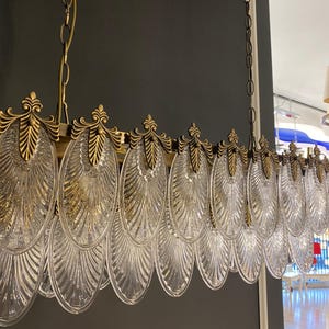 May include: A rectangular chandelier with a brass frame and clear, leaf-shaped glass pendants. The fixture is suspended from a chain and features ornate brass detailing. The design is elegant and suitable for interior lighting.
