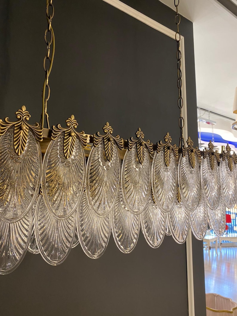 May include: A rectangular chandelier with a brass frame and clear, leaf-shaped glass pendants. The fixture is suspended from a chain and features ornate brass detailing. The design is elegant and suitable for interior lighting.