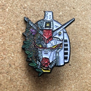 May include: A silver, red, and green enamel pin featuring a robot head with floral details. The robot head is half-covered in flowers and leaves.