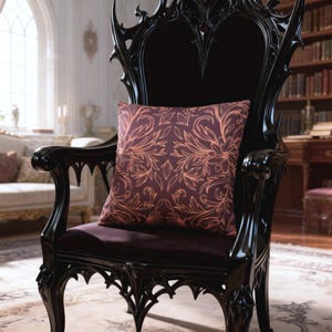 Puede incluir: Una silla negra y ornamentada con respaldo alto y tallas intrincadas. Un cojín cuadrado con un fondo morado oscuro y un patrón floral naranja repetido descansa sobre la silla. La silla está en una habitación con una biblioteca.