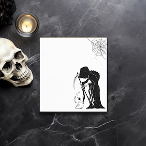 May include: A square, white canvas print featuring a black and white illustration of the Grim Reaper with a scythe and a small, cartoonish creature. A spiderweb is in the upper right corner. A skull and candle are in the background.