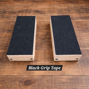 May include: Two rectangular wooden blocks with black grip tape on top. The blocks are light-colored wood and are secured with small metal fasteners. The text "Black Grip Tape" is displayed below the blocks.