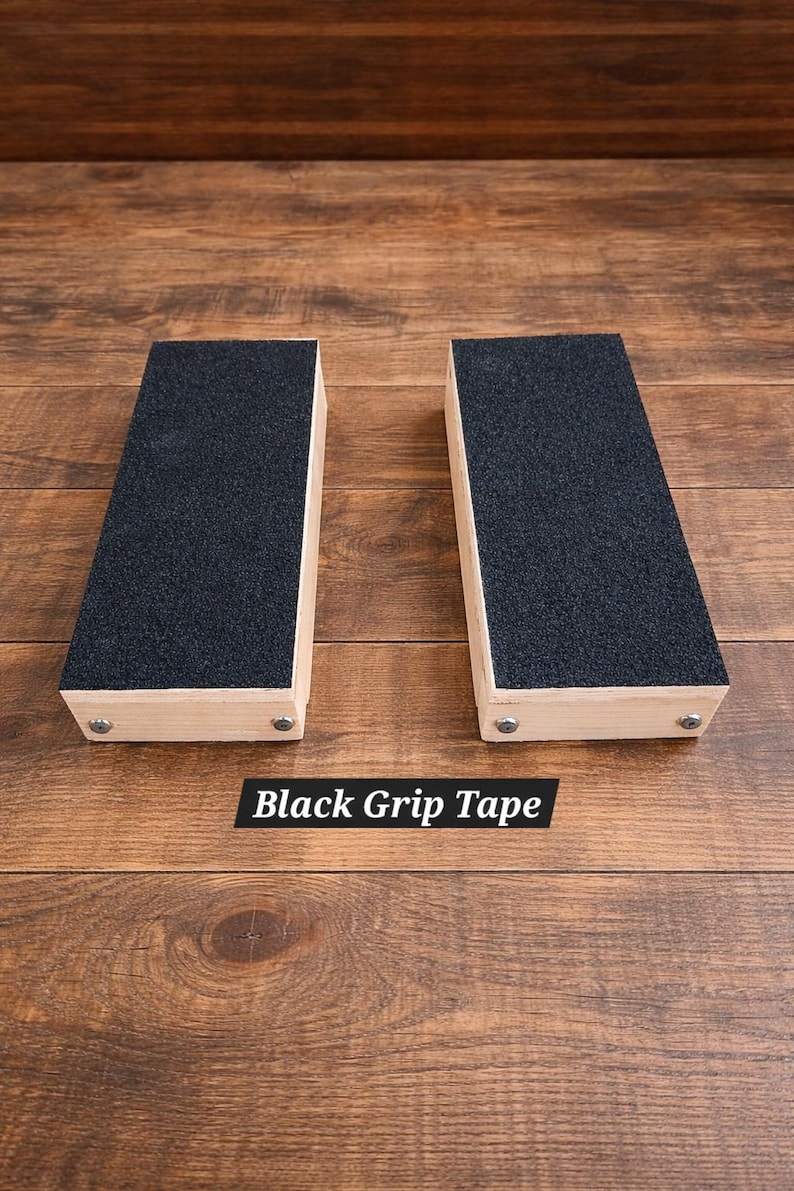May include: Two rectangular wooden blocks with black grip tape on top. The blocks are light-colored wood and are secured with small metal fasteners. The text "Black Grip Tape" is displayed below the blocks.