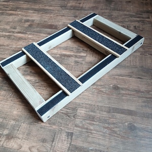 May include: A wooden balance board with a rectangular frame and a central crossbar. The frame and crossbar are made of light-coloured wood. The crossbar and frame have black, textured strips for grip.