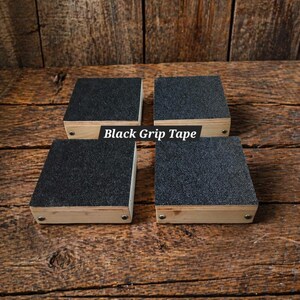 May include: Four square wooden blocks with black grip tape on top. The blocks are made of light-colored wood and are arranged on a wooden surface. The text "Black Grip Tape" is visible.