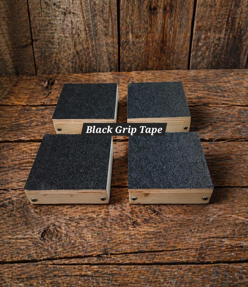 May include: Four square wooden blocks with black grip tape on top. The blocks are made of light-colored wood and are arranged on a wooden surface. The text "Black Grip Tape" is visible.
