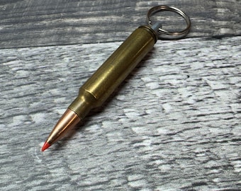 May include: A gold-colored bullet casing keychain with a silver key ring. The bullet casing has a red tip.