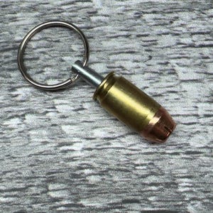 May include: A brass bullet casing keychain with a silver ring and a silver pin.