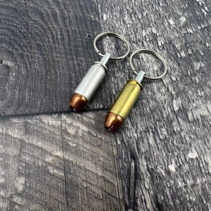 May include: Two bullet casing keychains, one silver and one gold, on a wooden background.