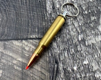 May include: A gold-colored bullet casing keychain with a silver ring. The bullet casing has a red tip.