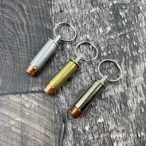 May include: Three bullet casing keyrings in silver, gold, and brass with copper tips. Each keyring has a silver ring.