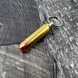 Op de afbeelding: Een gouden sleutelhanger in de vorm van een kogelhulzen met een zilveren ring. De huls heeft een koperkleurige punt.