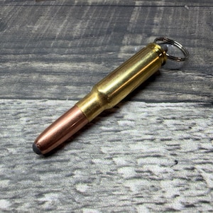 May include: A stylus shaped like a rifle cartridge featuring a metallic brass casing and a copper-colored bullet tip with a small black rubberized contact point at the end. A silver-toned metal split ring is attached to the base of the casing.