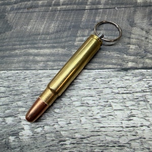 May include: A brass bullet-shaped keychain with a copper-coloured tip and a silver keyring. The bullet-shaped keychain is a unique accessory. The metallic finish gives it a rugged, industrial aesthetic.
