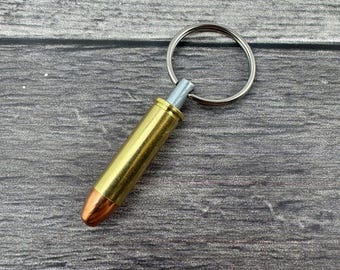 Könnte beinhalten: Ein Schlüsselanhänger aus einer goldfarbenen Patronenhülse mit einem silbernen Ring. Die Patronenhülse hat eine kupferfarbene Spitze.