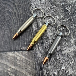 Puede incluir: Tres llaveros con forma de bala con diferentes acabados: plateado, dorado y negro. Cada llavero tiene un anillo dividido para sujetar las llaves.