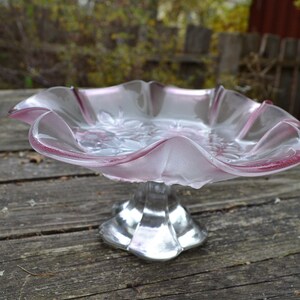 Könnte beinhalten: Ein gefrosteter Kuchenständer aus Glas mit einem gewellten Rand und einem silbernen Sockel. Der Ständer ist rosa und hat ein Blumenmuster.