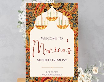 May include: A welcome sign for a Mehndi ceremony with a colorful paisley pattern border. The sign says "Welcome to Monica's Mehndi Ceremony" with the date "June 20, 2022" and the hashtag "#MonicaWedSricky".