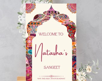 May include: Welcome to Natasha's Sangeet sign with a colorful patterned archway design. The sign is on a wooden easel and has the date May 2nd 2022 and the hashtag #NATIFOUNDMAT.