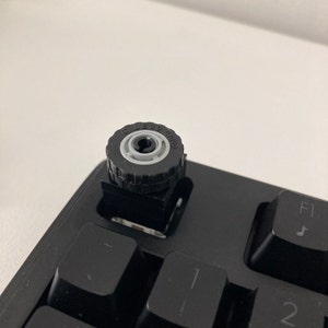Peut inclure: Un clavier noir avec un capuchon de touche en brique LEGO représentant un pneu noir avec le texte "LEGO ROUND" imprimé dessus.