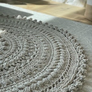 May include: A round, gray crocheted rug with a textured design. The rug has a fringe border.