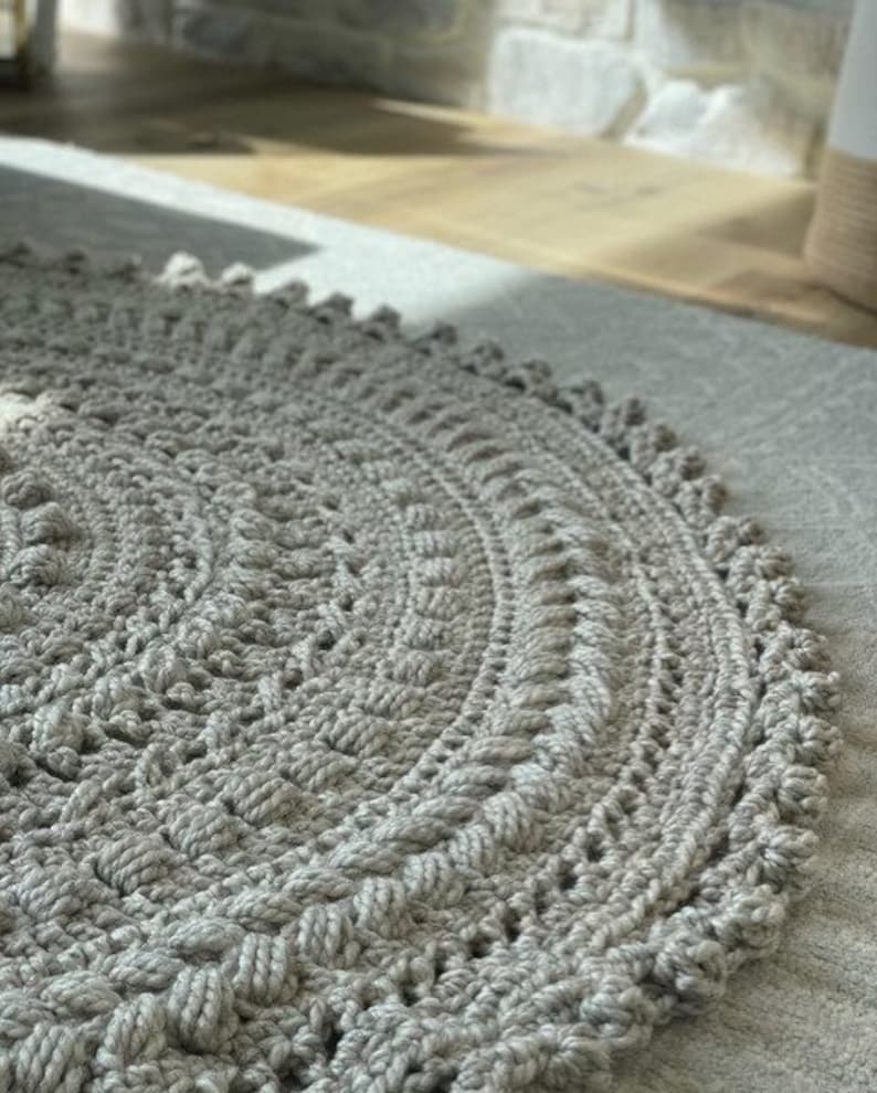 May include: A round, gray crocheted rug with a textured design. The rug has a fringe border.