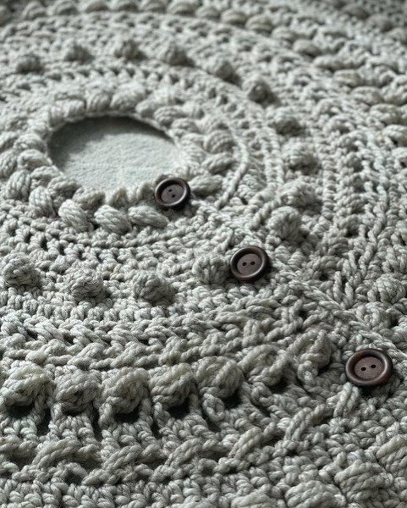 May include: Close-up of a gray crocheted fabric with three brown buttons. The fabric has a textured, bumpy surface.