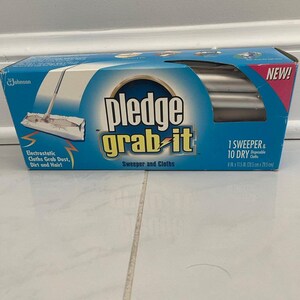 May include: A blue and white Pledge Grab-It sweeper and cloths box featuring the text Pledge Grab-It, 1 Sweeper & 10 Dry Disposable Cloths, and 8 in x 11.5 in. The packaging displays an illustration of a floor sweeper and electrostatic cloths.