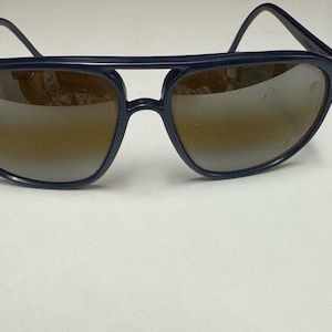 May include: Dark navy blue aviator sunglasses featuring a double bridge design and brown gradient lenses. The frames are constructed from a smooth, solid-colored material with thin temples that curve at the ends. The word FRANCE is visible on the arm.