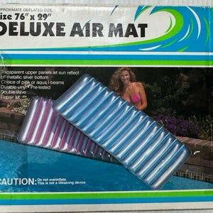 May include: A rectangular Deluxe Air Mat in blue and pink with a ribbed surface design. The packaging displays the text Size 76 inches by 29 inches, Deluxe Air Mat, and Caution: Do not overinflate. This is not a lifesaving device.