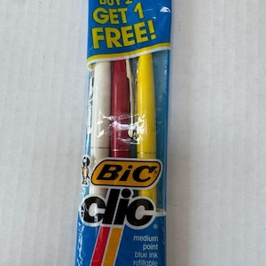 May include: A package of Bic Clic pens in a blue wrapper. The package contains a white, red, and yellow pen. The text "BUY 2 GET 1 FREE!" is at the top. The pens have medium point, blue ink, are refillable, and retractable.