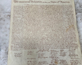 Op de afbeelding: Een rechthoekig perkamentdocument met de titel In Congress, July 4, 1776, The unanimous Declaration of the thirteen united States of America. Het papier heeft een verouderde, gebroken witte kleur met dichte zwarte cursieve tekst en talloze handtekeningen.