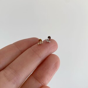 Pu&ograve; includere: Due piccoli orecchini a lobo con perno piatto, uno color oro e uno color argento. Ogni orecchino presenta un design a barra orizzontale con tre minuscole pietre chiare e scintillanti disposte in fila sulla superficie frontale.