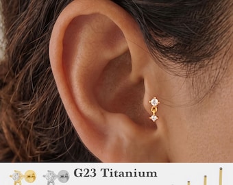 Könnte beinhalten: Ein goldfarbener Hängeohrring mit zwei kleinen klaren Steinen in vertikaler Anordnung. Der Text G23 Titanium, 16g, 18g, 20g sowie 5mm, 6mm, 8mm, 10mm ist sichtbar, zusammen mit Abbildungen von goldenen und silbernen Steckern und Stablängen.
